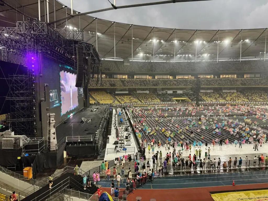 Concert venue featuring a large stage and scattered audience under cloudy skies.