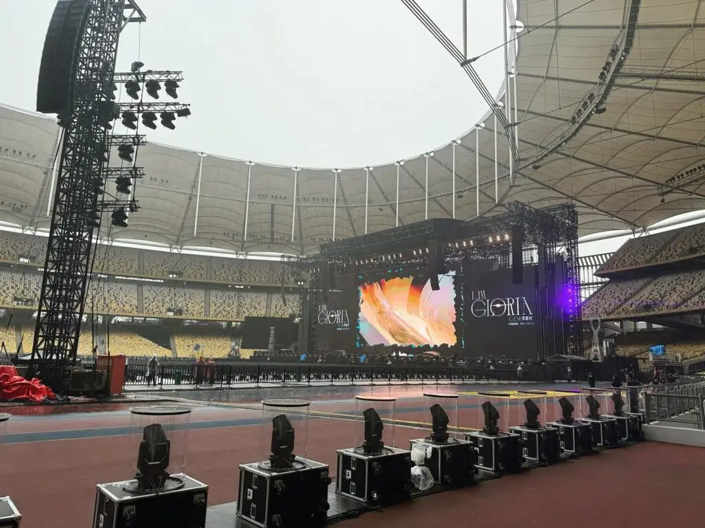 Concert stage setup with large screen and lighting equipment in an empty stadium.