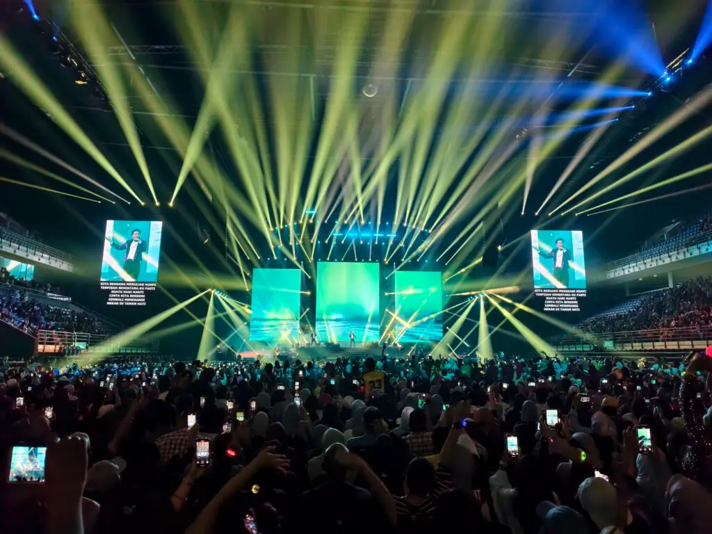 A concert scene featuring bright stage lights and an audience holding phones in a large venue.
